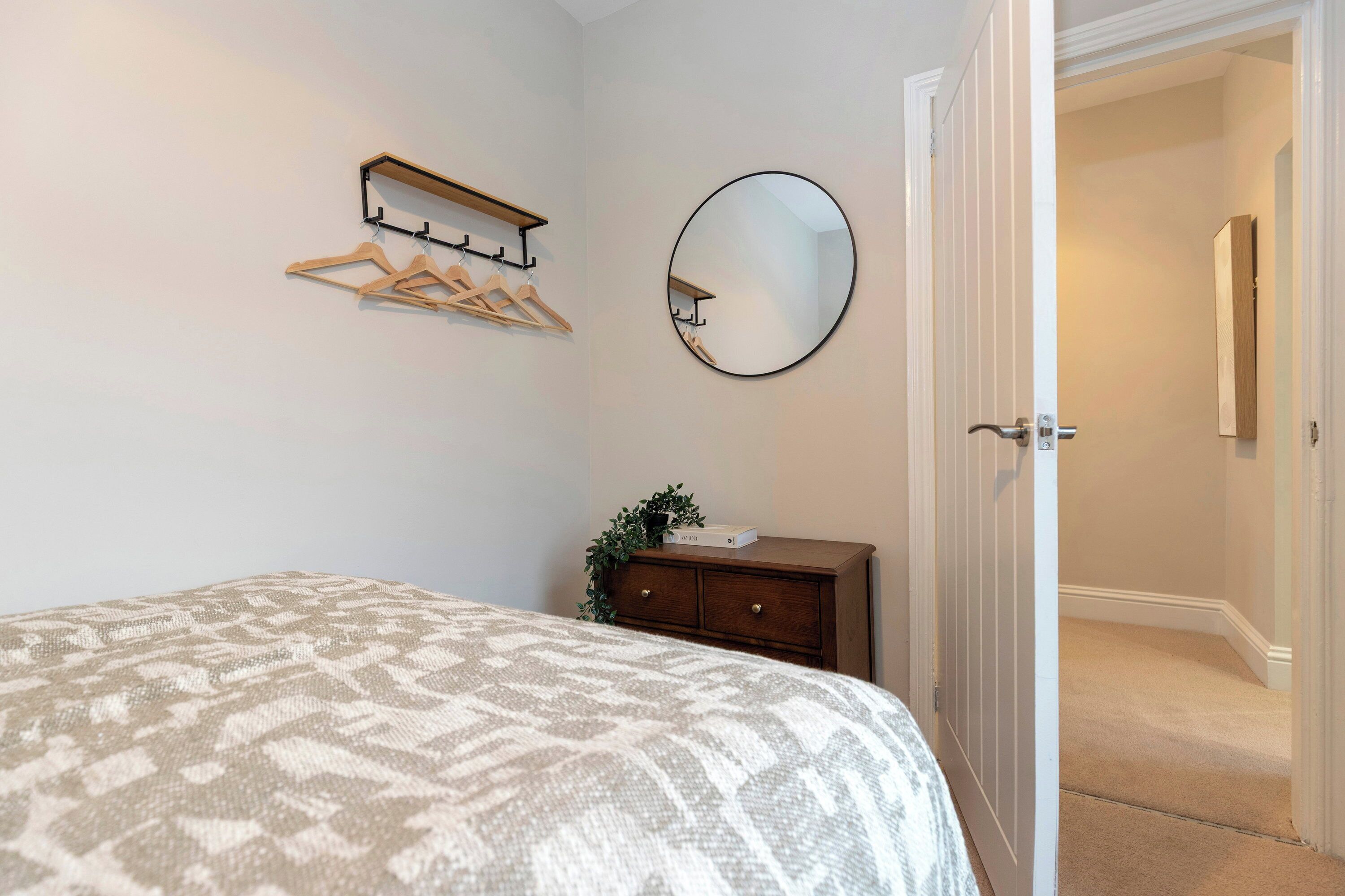 A bedroom with a bed, a dresser, a mirror, and a coat rack.