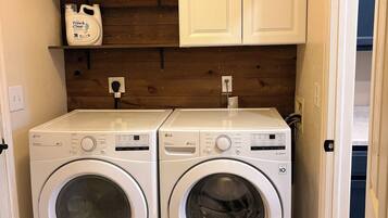 A laundry room with two white LG front-loading washing machines, a wooden wall, and a white cabinet above.