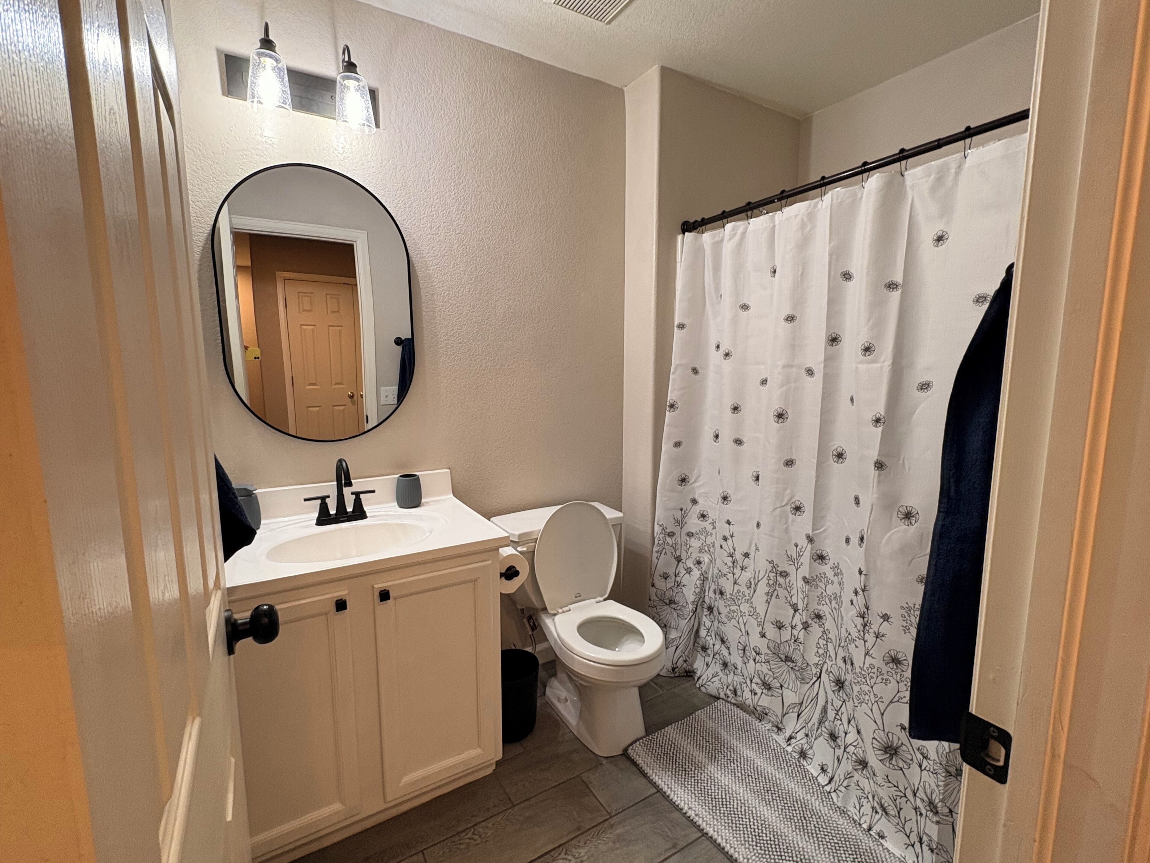 Un baño con lavamanos blanco, inodoro, espejo y cortina de ducha con estampado floral.
