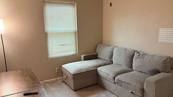 A living room with a sectional sofa, a small table, a lamp, and a window with blinds.