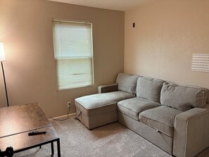 A living room with a sectional sofa, a small table, a lamp, and a window with blinds. - 3-bedroom townhome in tranquil Northglenn, 25 minutes from Denver (Northglenn)