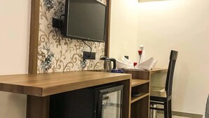 Habitación de hotel con un escritorio de madera, un televisor montado en la pared, un refrigerador pequeño y una zona de comedor con una silla y una mesa.