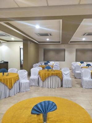 Un salón de conferencias con mesas redondas, sillas blancas y manteles amarillos.