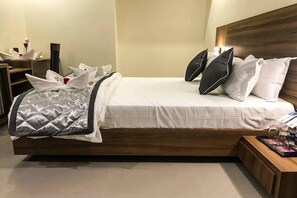 Una cama bien hecha con almohadas y una colcha, una mesita de noche con una bandeja de objetos y un cabecero de madera.