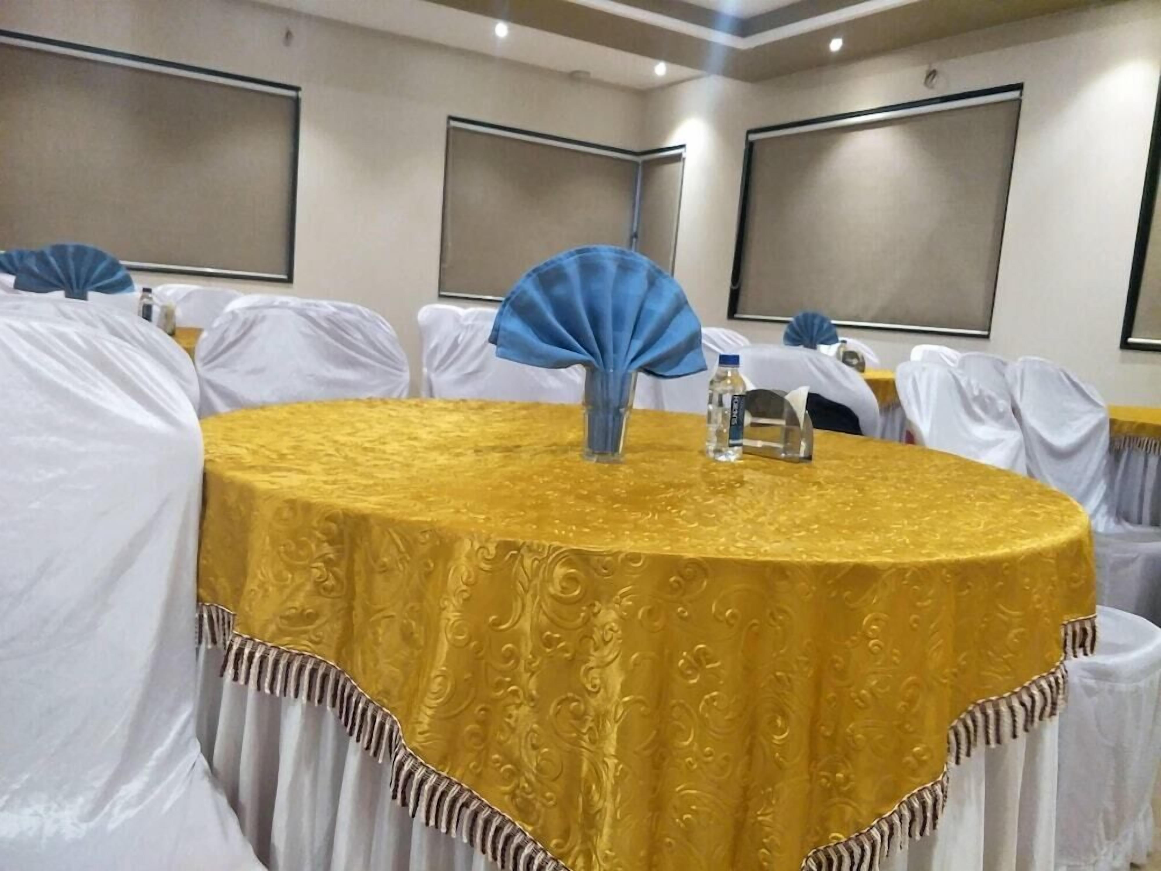 A conference room with a round table covered in a golden tablecloth, white chairs, and a blue fan on the table.