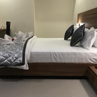 Una cama bien hecha con una manta de color gris y blanco con estampado, almohadas blancas y un cabecero de madera.