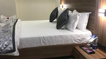 A hotel room with a bed, pillows, a bedside table with a water bottle, and a tray with a card and glasses.