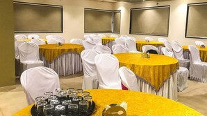 Un salón de conferencias con varias mesas y sillas, cada una con mantel dorado y fundas blancas para las sillas.
