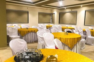 Un salón de conferencias con varias mesas y sillas, cada una con mantel dorado y fundas blancas para las sillas.