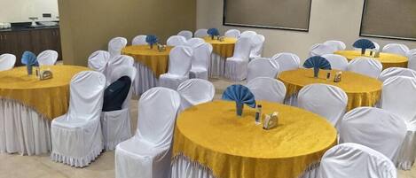 A conference room with round tables and chairs, some with yellow tablecloths and white chair covers.
