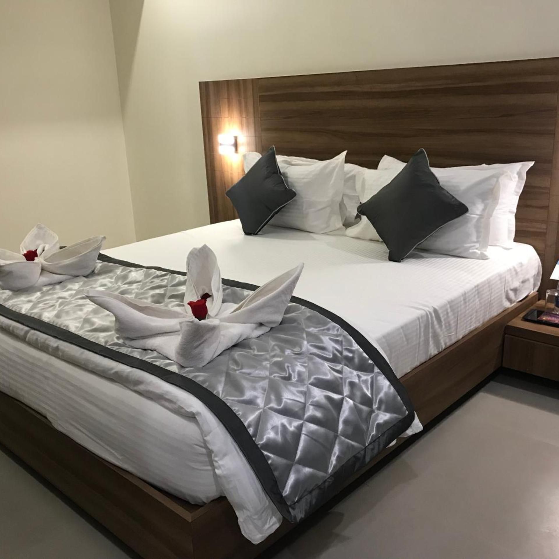 A hotel room with a neatly made bed, a wooden headboard, and a bedside table with a lamp.