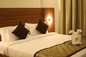 Una cama bien tendida con almohadas blancas y oscuras, una colcha acolchada y una toalla pequeña con un diseño floral sobre una mesita de noche.