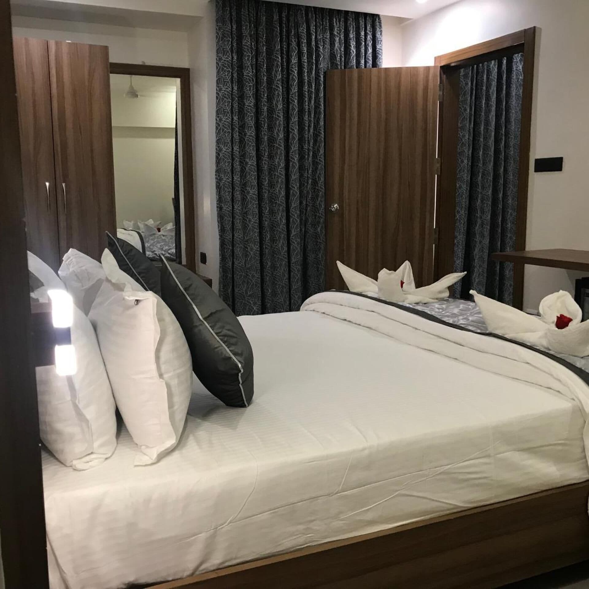 A hotel room with a large bed, a wardrobe, a mirror, and curtains.