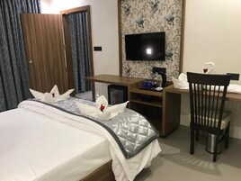 A hotel room with a bed, a desk with a computer, a television, and a chair.