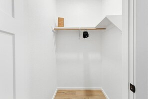 Ein kleiner Raum mit weißen Wänden, Holzboden, einer weißen Tür und einem Regal mit einem einzelnen Gegenstand.