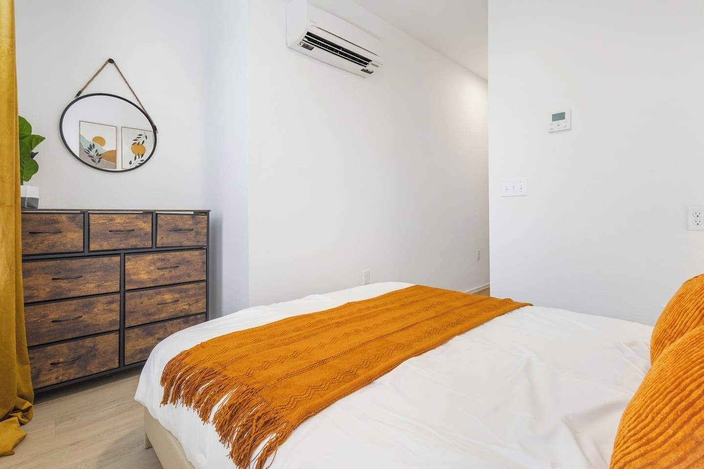 A bedroom with a bed, a dresser, an air conditioning unit, and a wall-mounted thermostat.