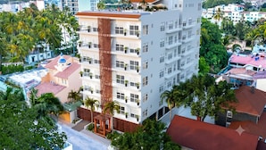 Un hotel de varios pisos con balcones, rodeado de palmeras y otros edificios.