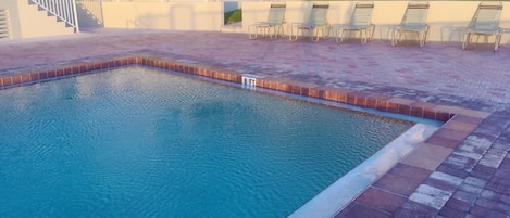 Ein Schwimmbecken mit einer Tiefenmarkierung von 2,4 Metern, umgeben von einer gefliesten Liegefläche und Liegestühlen.