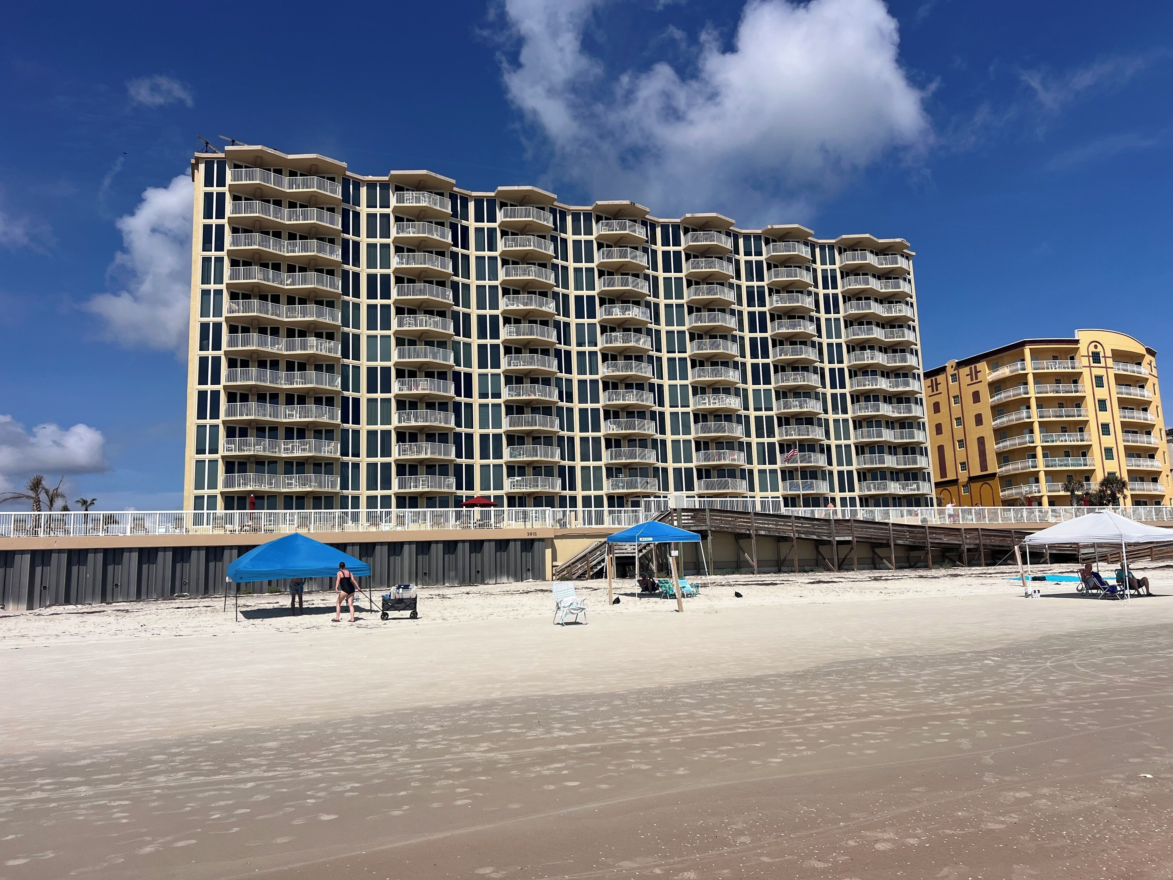 A beachfront hotel with multiple balconies, a sandy beach, and a clear blue sky.