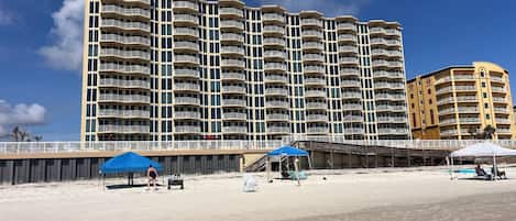 A beachfront hotel with multiple balconies, a sandy beach, and a clear blue sky.