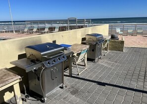 An outdoor patio with two barbecue grills, a table, and chairs facing a beach. - #207 3BR 3.5BA  Direct Ocean, Full Remodel, 2K + 2Q, Indoor Laundry, Gorgeous (Daytona Beach Shores)