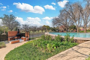A pool area with a barbecue setup and a brick structure. - Golf-View Apt in Circa Illovo, Sandton (Sandton)