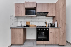 A compact kitchen with a built-in microwave, stove, and oven, featuring wooden cabinetry and white subway tiles. - Golf-View Apt in Circa Illovo, Sandton (Sandton)
