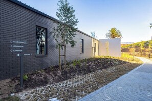 A modern building with a brick facade, directional signage, and a landscaped area with young trees and a palm. - Modern Luxury at Park Place by Ctha (Cape Town)