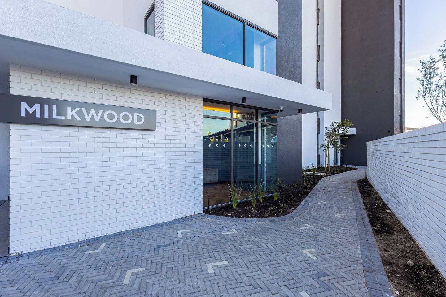 Un bâtiment moderne, sur lequel on peut lire l’inscription « MILKWOOD », et un chemin pavé menant à une entrée en porte de verre.