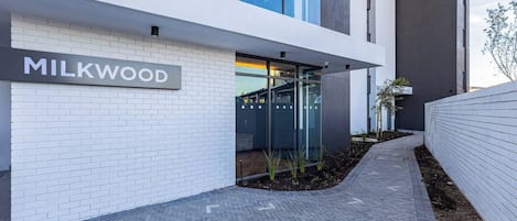 A modern building with a sign reading 'MILKWOOD' and a paved walkway leading to a glass door entrance.