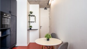 A compact kitchen with a built-in oven, a dining table with chairs, and a small potted plant on the table. - The Urban Nest by CTHA (Cape Town)