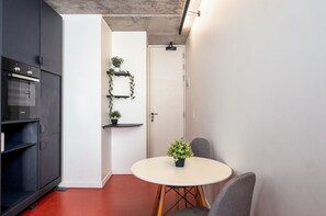 A compact kitchen with a built-in oven, a dining table with chairs, and a small potted plant on the table. - The Urban Nest by CTHA (Cape Town)