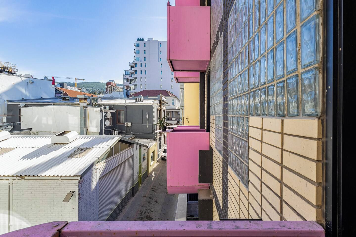 Um beco estreito entre edifícios, com uma estrutura rosa à direita e um prédio branco à esquerda.