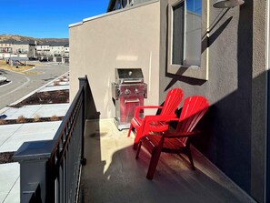 A balcony with a barbecue grill, red chairs, and a view of a street and buildings. - Ski Haven Hideaway 15 Mins to Park City Slopes (Hideout)