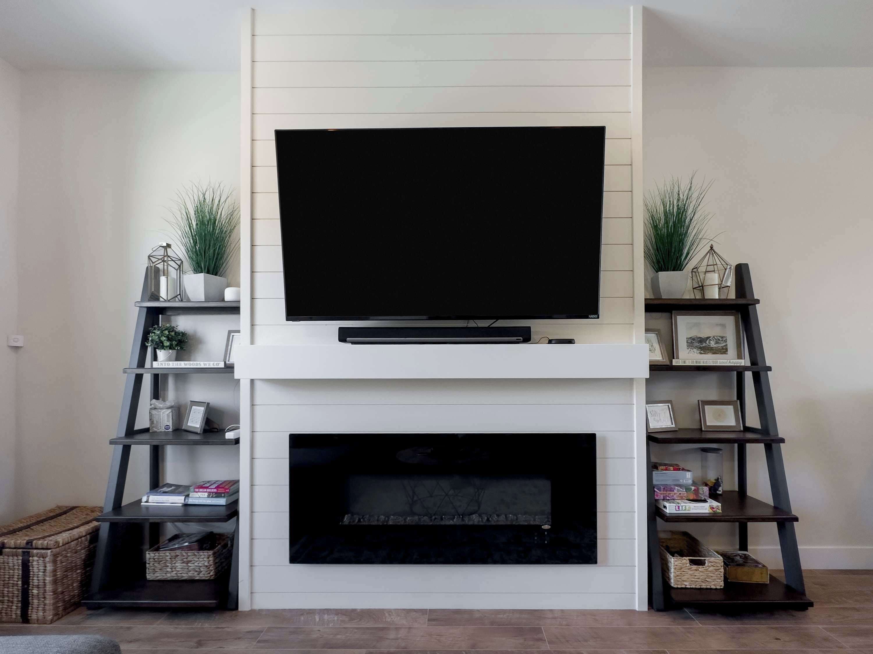 Ein modernes Wohnzimmer mit Flachbildfernseher über einem Kamin, beiderseits stehen Regale mit dekorativen Gegenständen und Büchern.