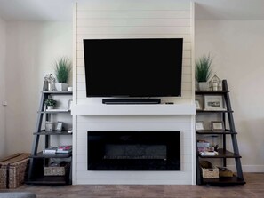 A modern living room with a flat-screen TV mounted above a fireplace, flanked by two shelving units with decorative items and books. - Ski Haven Hideaway 15 Mins to Park City Slopes (Hideout)