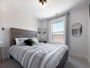 Ein Schlafzimmer mit einem Bett, einem Nachttisch, einem Fenster und einem Spiegel.