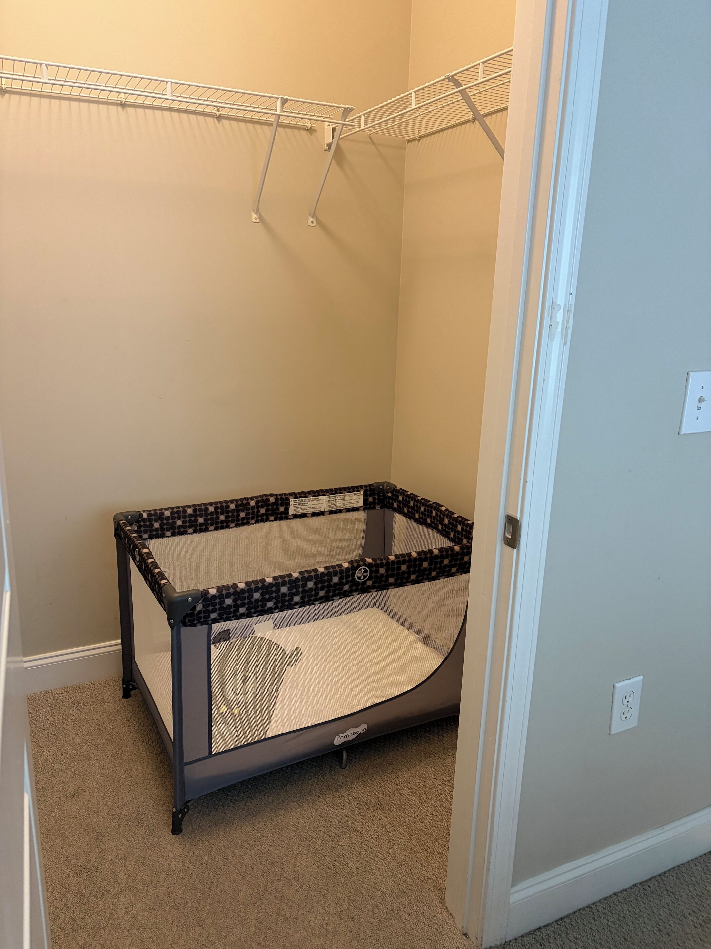 Ein Zimmer mit einem Reisebett in der Ecke, einer weißen Tür und einem Wandregal.