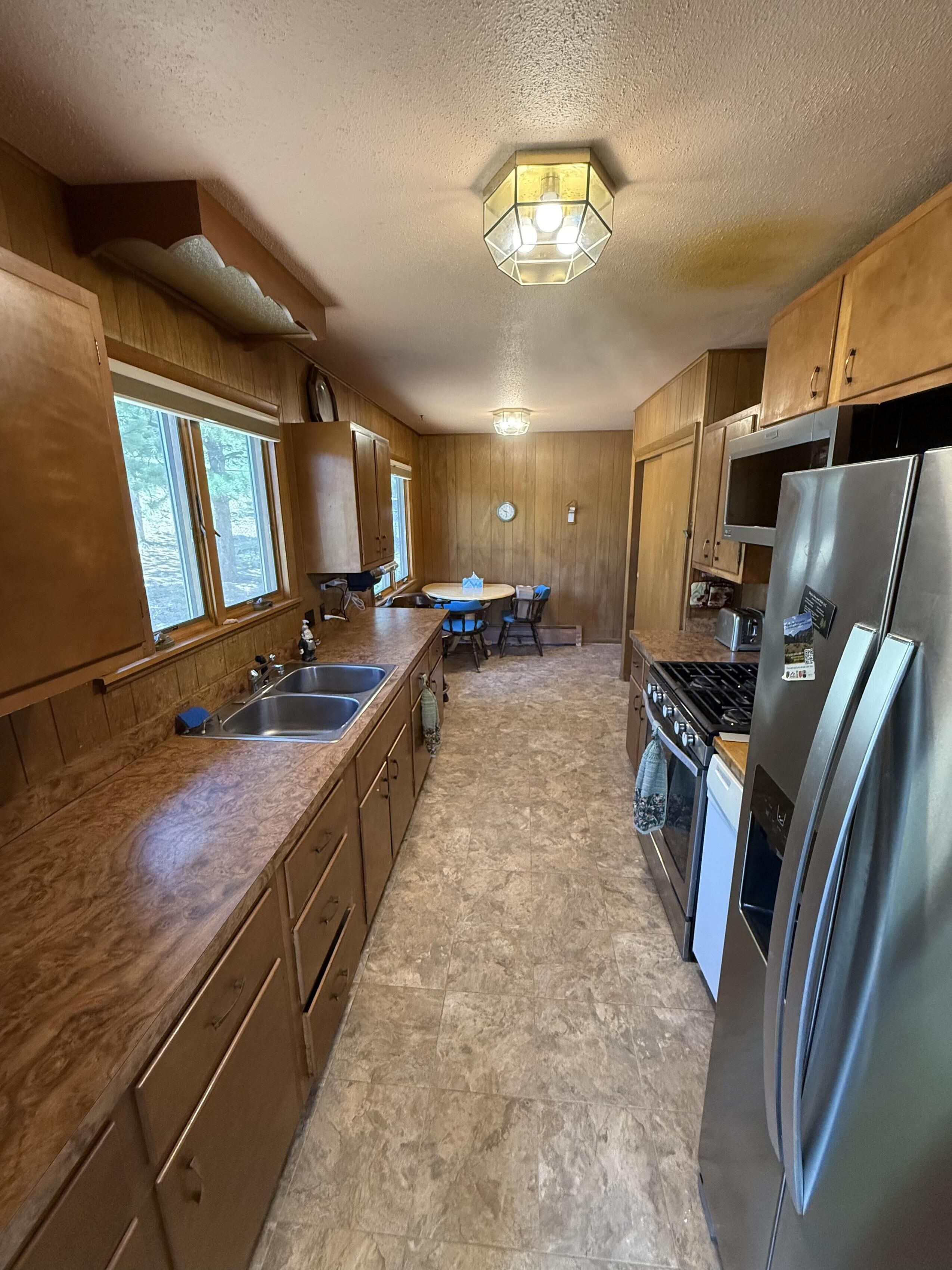Une cuisine avec des meubles en bois, un réfrigérateur en acier inoxydable, une cuisinière et une fenêtre avec des stores.