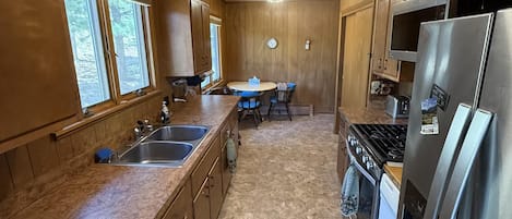 A kitchen with wooden cabinets, a stainless steel refrigerator, a stove, and a window with blinds.