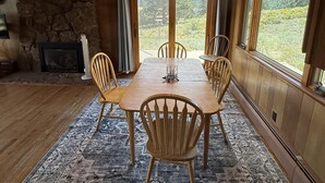 Un comedor con una mesa y sillas de madera, una alfombra estampada, un muro de piedra y una chimenea.