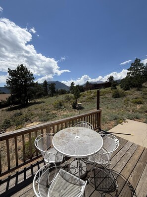 Eine Terrasse mit einem runden Metalltisch und Stühlen, mit Blick auf eine gebirgige Landschaft.