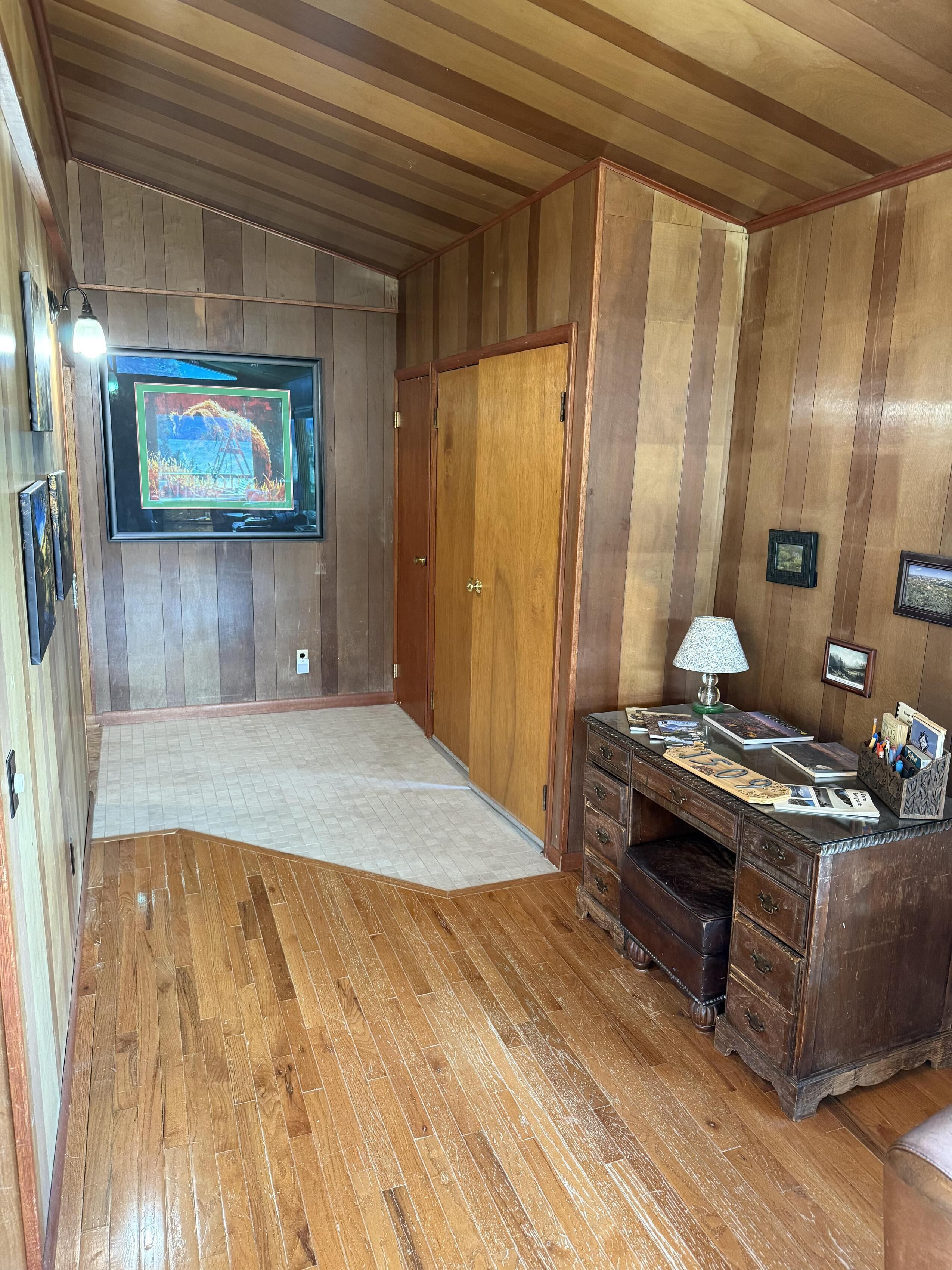 A room with wooden paneling, a television mounted on the wall, a desk with a lamp, and a large rug on the floor.