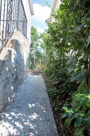 A narrow concrete pathway flanked by dense foliage and a metal fence. - Near NYC & Metro-North! Private Yonkers Studio (Yonkers)