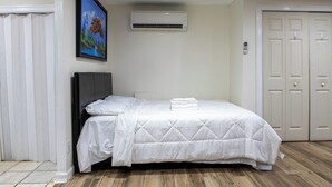 A bedroom with a bed, a wall-mounted air conditioner, a painting, and a set of doors. - Near NYC & Metro-North! Private Yonkers Studio (Yonkers)