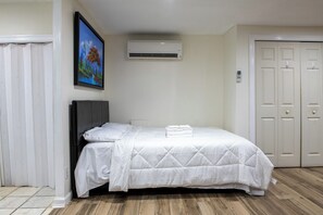A bedroom with a bed, a wall-mounted air conditioner, a painting, and a set of doors.