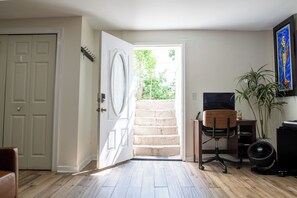 A room with a wooden floor, a desk with a chair, a door leading to a staircase, and a plant.