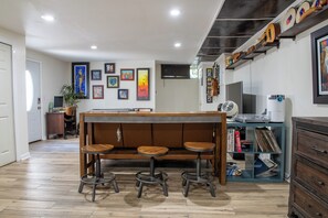Ein Zimmer mit einer Holzbank, Hocker, einem Bücherregal und gerahmten Kunstwerken an der Wand.