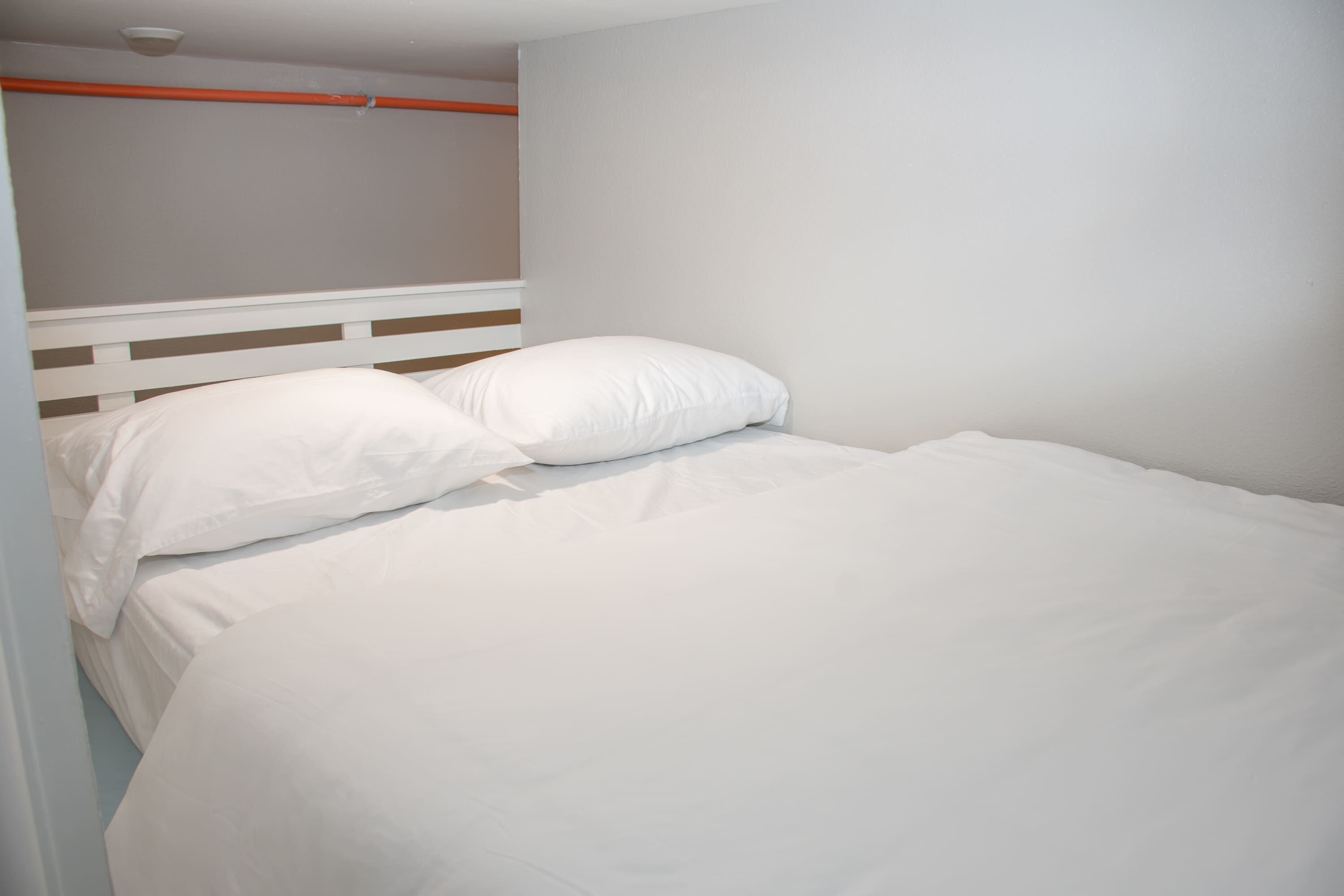 A single bed with white bedding and pillows, a white headboard, and a plain wall.