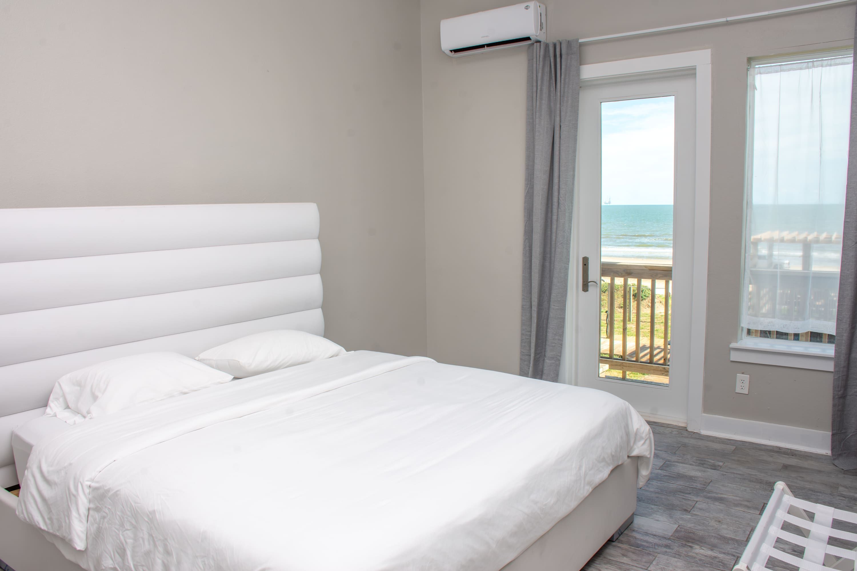 A bedroom with a large bed, a view of the beach, and an air conditioning unit.